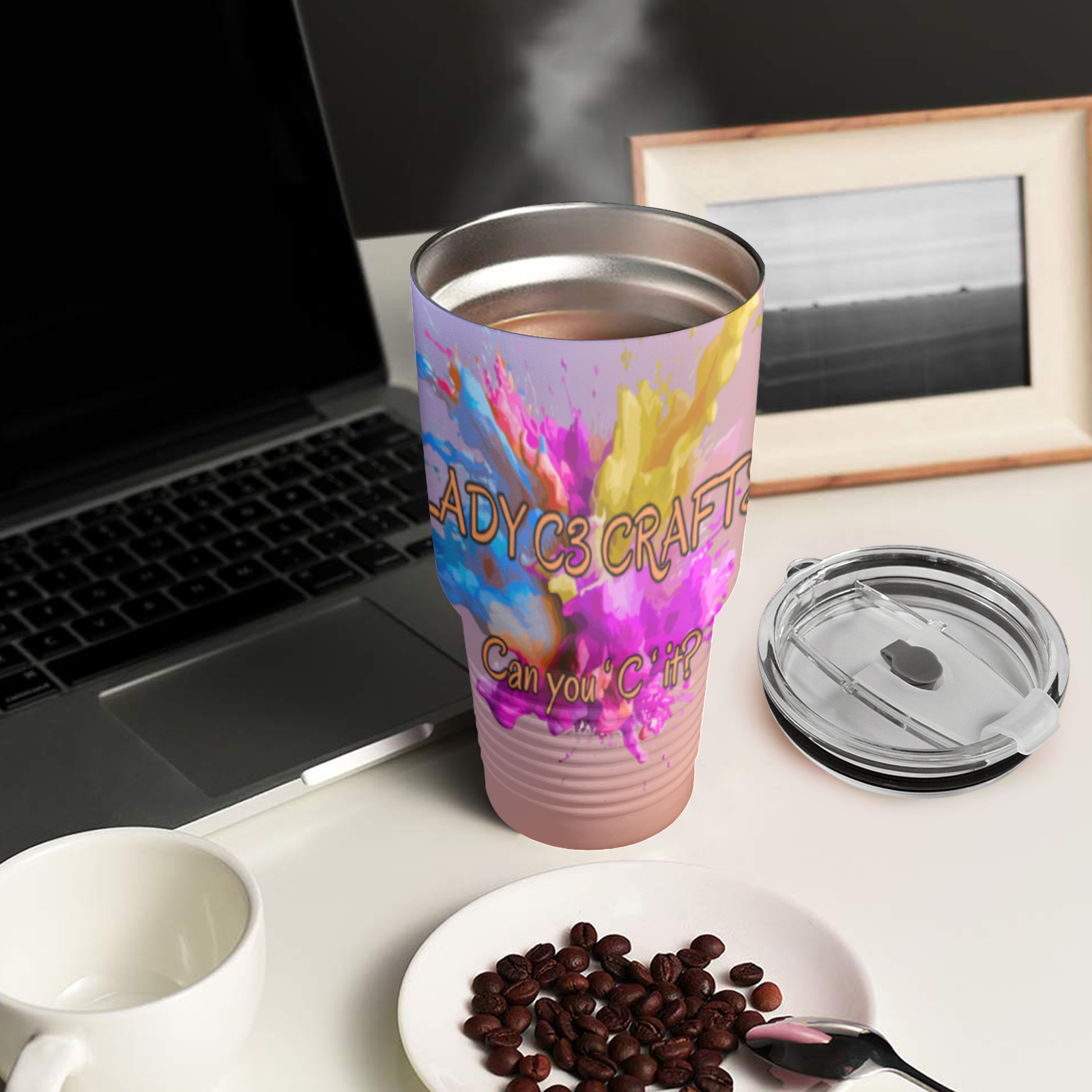 Colorful tumbler with text on a desk next to a laptop and coffee beans.