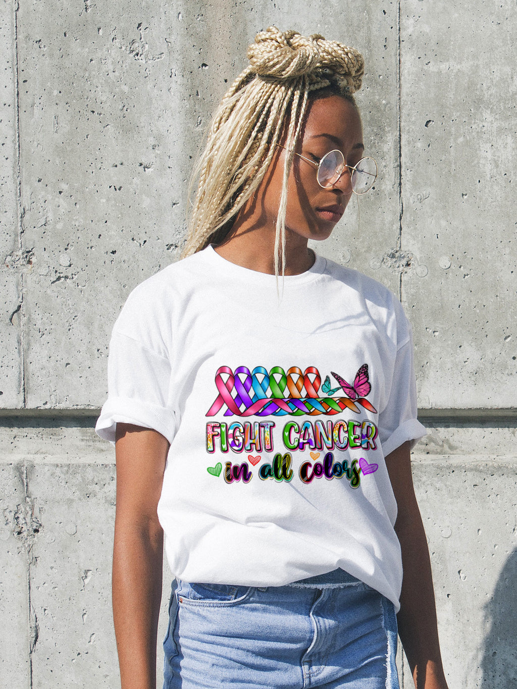 Person wearing a white t-shirt with colorful cancer awareness design against a concrete wall.