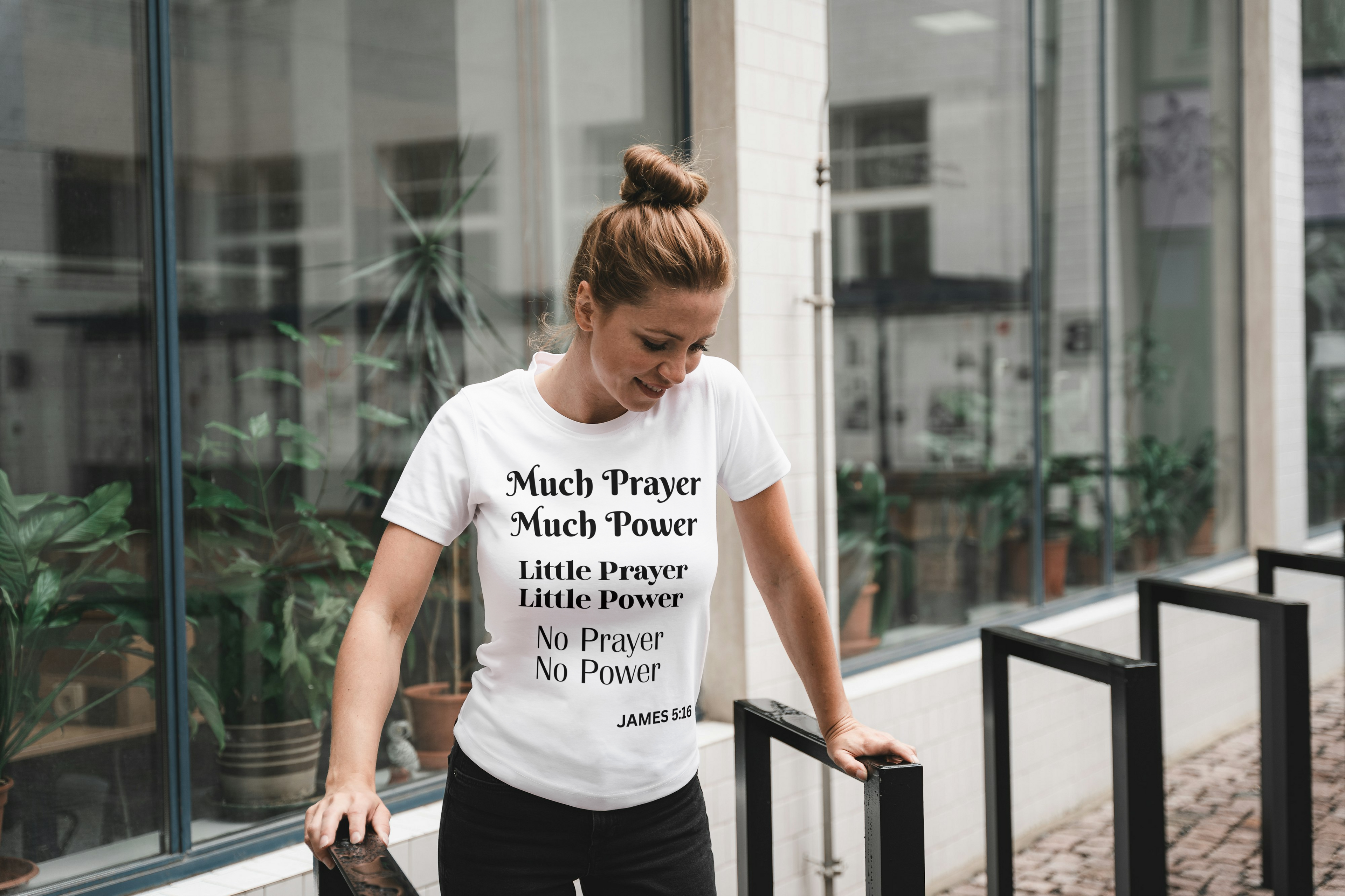 Woman wearing a white t-shirt with motivational quote, standing outdoors near glass doors.