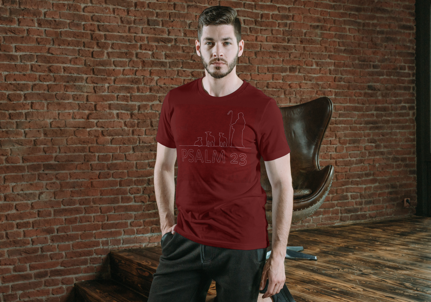 Man wearing a red t-shirt with text standing against a brick wall.